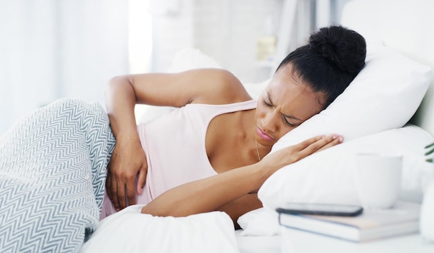 Je ne peux même pas dormir à travers cette douleur Photo d'une jolie jeune femme souffrant de crampes d'estomac alors qu'elle était allongée dans son lit à la maison