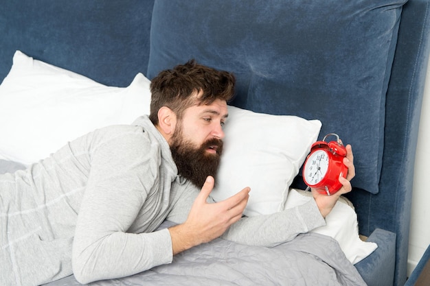 Je ne peux pas supporter le bruit Les soins de santé ont besoin de plus de détente au lit homme stressé et malheureux homme barbu hipster envie de dormir réveil du matin déteste le bruit du réveil Étapes du sommeil Homme à la maison