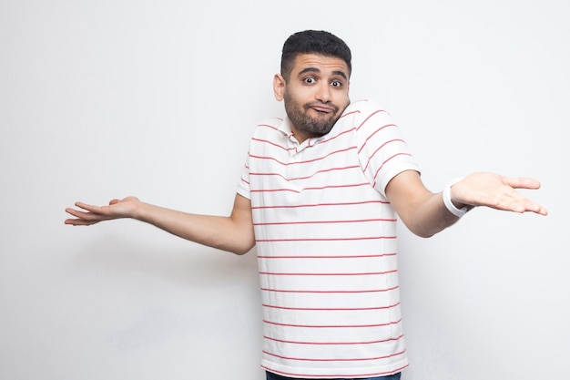 Je ne sais pas. Portrait d'un beau jeune homme barbu confus en t-shirt rayé debout avec les bras levés et ne sait pas quoi faire. tourné en studio intérieur, isolé sur fond blanc.