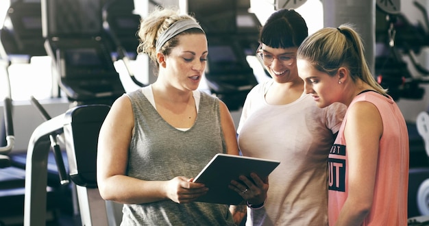 Je peux suivre toutes mes cibles et mes objectifs Photo recadrée de trois jeunes femmes sportives regardant une tablette numérique dans la salle de sport