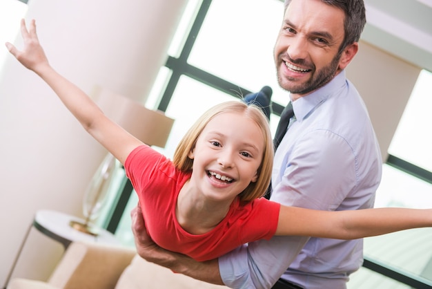 Je peux voler! Heureux père en tenue de soirée jouant avec sa fille à la maison