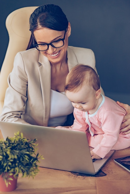 Je peux vous aider! Vue de dessus d'une petite fille utilisant un ordinateur portable alors qu'elle était assise sur un bureau avec sa mère au bureau