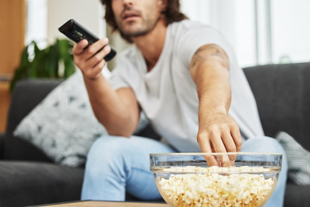 Je pourrais manger tout ce bol sans que personne ne regarde Plan d'un homme assis sur le canapé en train de manger du pop-corn et de regarder la télévision