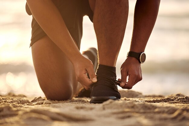 Je prends le chemin de la victoire aujourd'hui Gros plan d'un homme méconnaissable attachant ses lacets tout en faisant de l'exercice à la plage