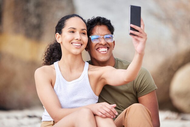 Je resterai à vos côtés à travers n'importe quoi Photo d'un jeune couple prenant un selfie à la plage