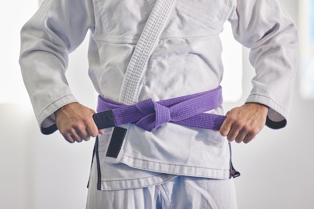 Je suis une ceinture violette Photo recadrée d'un homme méconnaissable attachant une ceinture violette autour de la taille hist en plein jiu jitsu gi