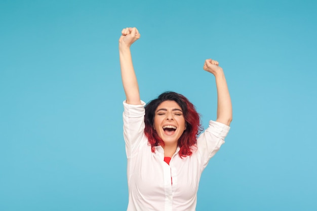 Je suis championne Portrait d'une femme énergique et enthousiaste avec des cheveux roux fantaisie en chemise levant les mains et criant de la réussite gagnante de la vie heureuse prise de vue en studio isolée sur fond bleu