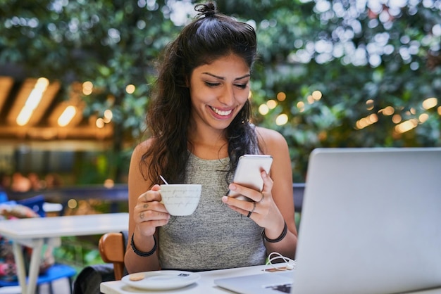 Je suis dans ce café cool avec le meilleur café Photo d'une jeune femme utilisant un téléphone portable et un ordinateur portable dans un café