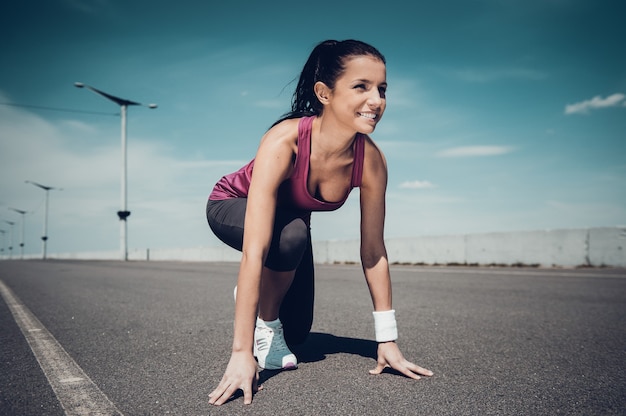 Je suis prêt! Belle femme en chaussures de sport debout dans la ligne de départ et souriant