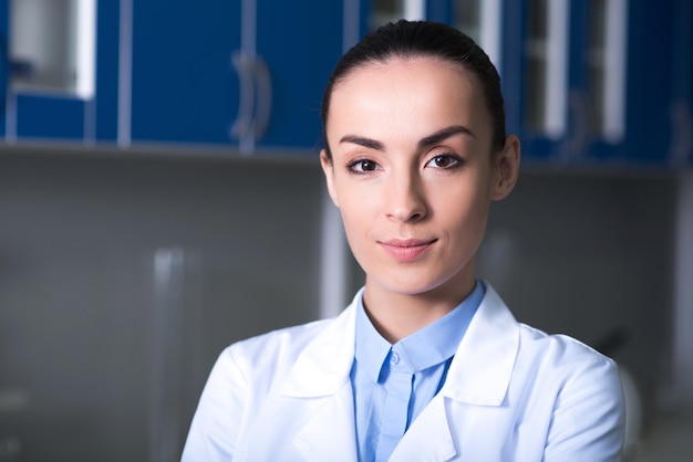 Je suis un professionnel Jeune scientifique assez sûr de lui debout dans la pièce dans une blouse de laboratoire regardant droit et ressemblant à assuré