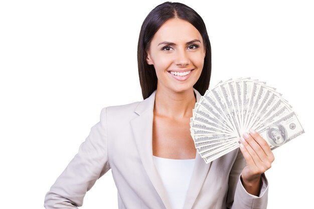 Je suis riche! Jeune femme d'affaires confiante en costume montrant de l'argent et souriant en se tenant debout sur fond blanc