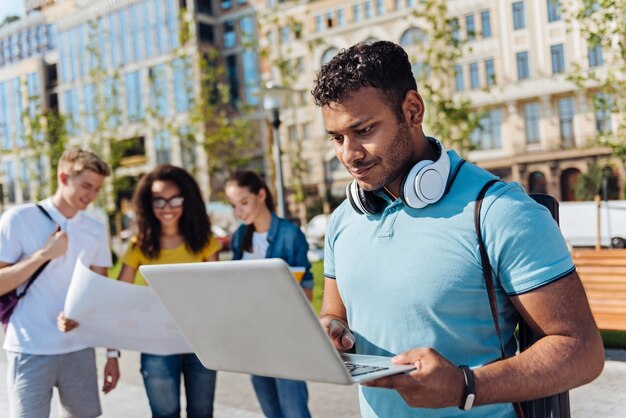 Je suis sérieux. Séduisante jeune homme debout en position semi sur le premier plan et en appuyant sur les lèvres tout en regardant l'écran de son ordinateur portable