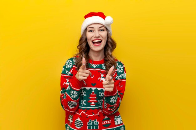 Je te choisis, jeune fille en pull de Noël et chapeau de père Noël, sourit et montre la caméra