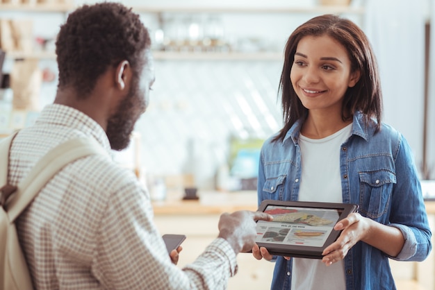 Je veux celui-ci. Jolie jeune femme tenant une tablette avec menu de cafés et le montrant à son amie tandis que l'homme pointant sur le plat de son choix