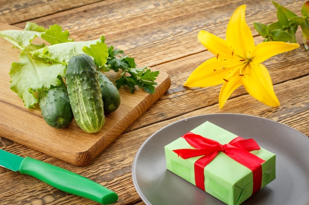 Je viens de cueillir des concombres et de la salade verte sur une planche à découper, un couteau, une assiette avec boîte-cadeau et une fleur de lys sur de vieilles planches en bois. Juste des légumes récoltés. Vue de dessus.