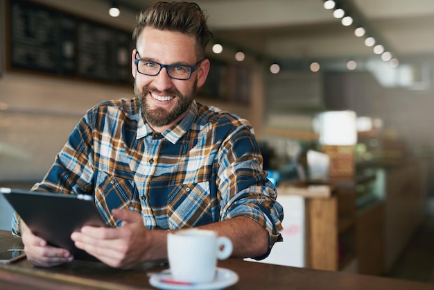 Je viens pour le wifi mais les cafés bien aussi Portrait d'un jeune homme utilisant sa tablette assis près de la fenêtre dans un café