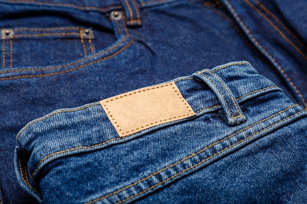Jean en denim bleu avec étiquette emty. Étiquette d'étiquette en cuir blanc marron sur fond de pantalon en jean. Étiquette en cuir beige maquette vierge. Fermer.