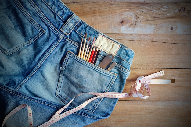 Jeans avec mesure et crayons, pinceaux dans la poche arrière sur bois