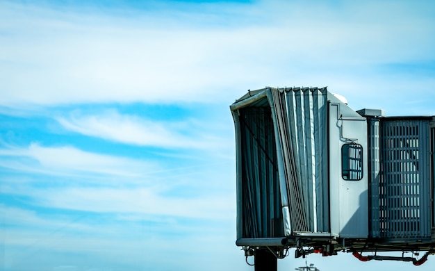 Jet bridge après le décollage d'une compagnie aérienne commerciale à l'aéroport contre le ciel bleu et les nuages blancs. Pont d'embarquement des passagers d'aéronef amarré. Pont jet vide.