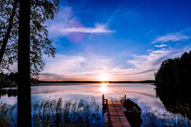 Jetée en bois avec bateau de pêche au coucher du soleil sur un lac en Finlande rurale