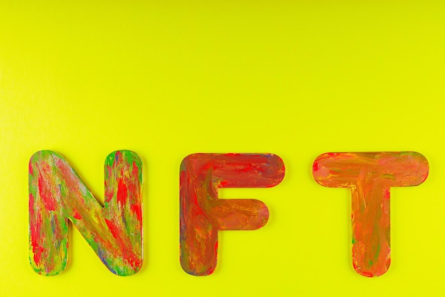 Jeton non fongible. Acronyme NFT de lettres multicolores sur fond jaune. Concept d'art cryptographique. Espace de copie. Vue de dessus