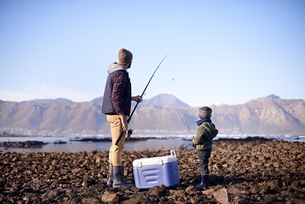 Jetons-le dans les profondeurs Photo d'un père et de son fils debout avec leurs engins de pêche au bord de la mer