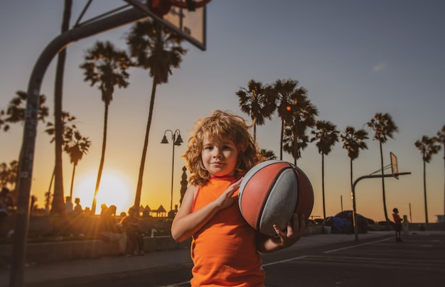 Jeu de basket pour enfants. Mignon petit garçon tenant un ballon de basket essayant de faire un score. Adorable enfant jouant au basket sur le terrain au coucher du soleil.