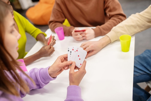 Jeu, processus. Jeune fille regardant ses cartes assis à table avec ses amis joueurs passant du temps libre