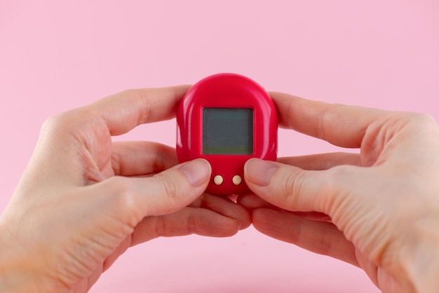 Jeu de Tamagotchi animal de compagnie virtuel dans les mains sur un fond rose