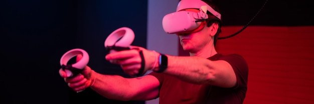 Jeu vr et joueur de réalité virtuelle s'amusant à jouer sur un jeu de tir vidéo de simulation futuriste dans des lunettes 3d et des joysticks dans une salle de divertissement vr avec technologie d'innovation et bannière lumineuse au néon