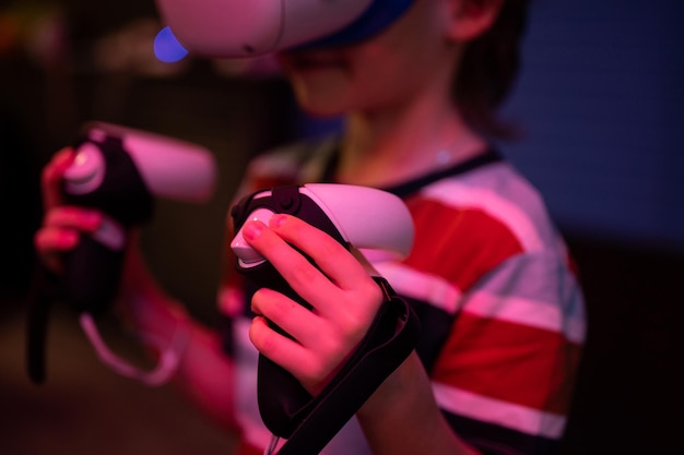 Jeu vr et réalité virtuelle kid boy gamer de six ans s'amusant à jouer sur un jeu vidéo de simulation futuriste dans des lunettes 3d et des joysticks dans une salle de divertissement vr avec technologie d'innovation et néon