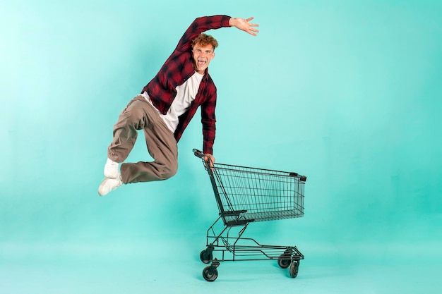 Un jeune acheteur fou saute et se réjouit avec un chariot d'achat du supermarché.