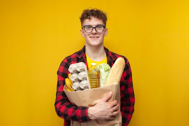 un jeune acheteur tient un paquet de produits et sourit sur fond jaune