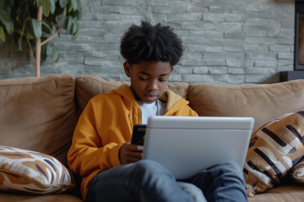 Un jeune adolescent afro-américain utilise un ordinateur portable pour discuter avec ses amis et utiliser les réseaux sociaux sur Internet s'assoit sur le canapé avec un ordinateur portatif sur les genoux Addiction numérique