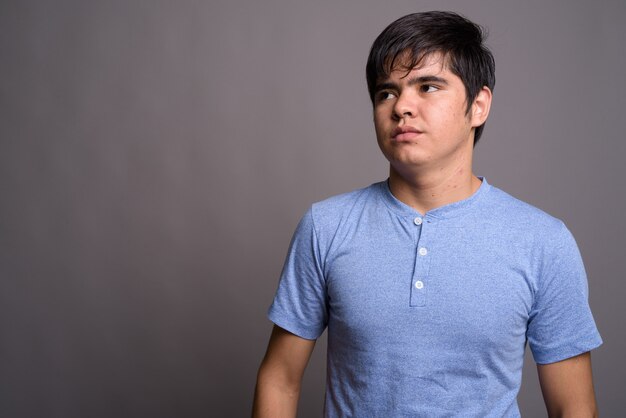 Jeune adolescent asiatique portant une chemise bleue contre un mur gris