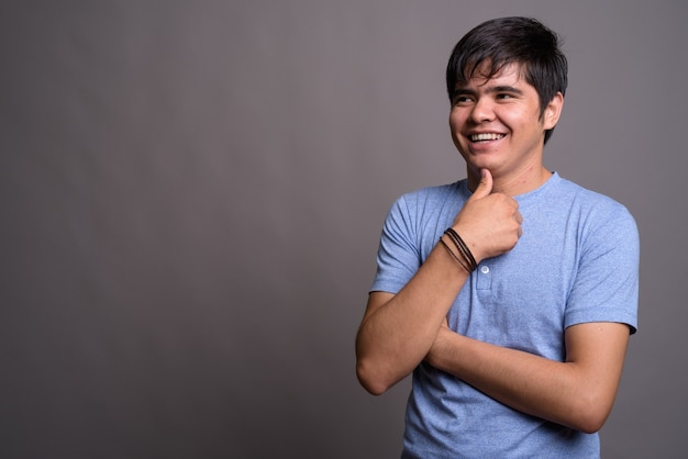 Jeune adolescent asiatique portant une chemise bleue contre un mur gris