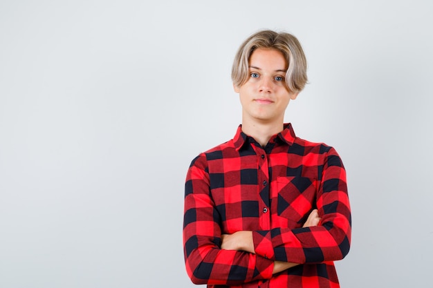 Jeune adolescent en chemise à carreaux tenant les bras croisés et l'air joyeux, vue de face.