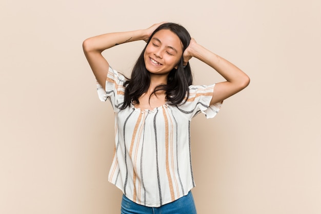 Jeune adolescent chinois mignon Jeune femme blonde portant un manteau contre un mur rose rit joyeusement en gardant les mains sur la tête. Concept de bonheur.