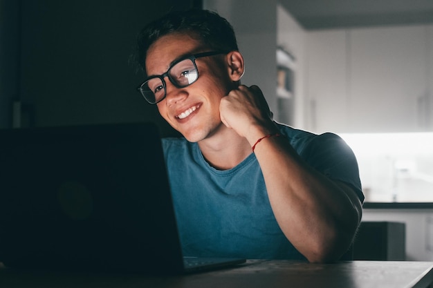 Un jeune adolescent étudie et travaille à la maison la nuit sur la table à l'aide d'un ordinateur portable souriant et s'amusant à faire ses devoirs Lumière de l'écran sur facexA