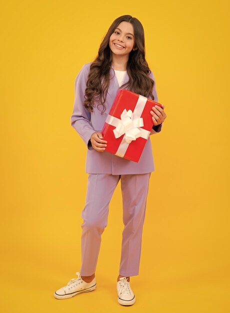 Jeune adolescent fille enfant tenant une boîte-cadeau isolée sur fond jaune Cadeau pour l'anniversaire des enfants