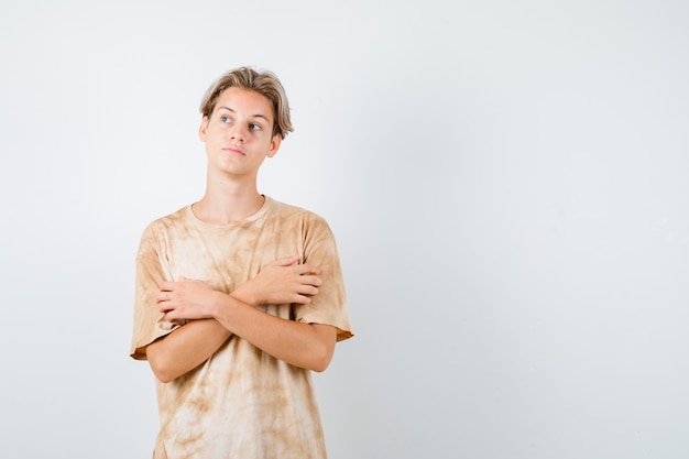 Jeune adolescent gardant les bras croisés sur la poitrine, regardant loin en t-shirt et l'air pensif, vue de face.