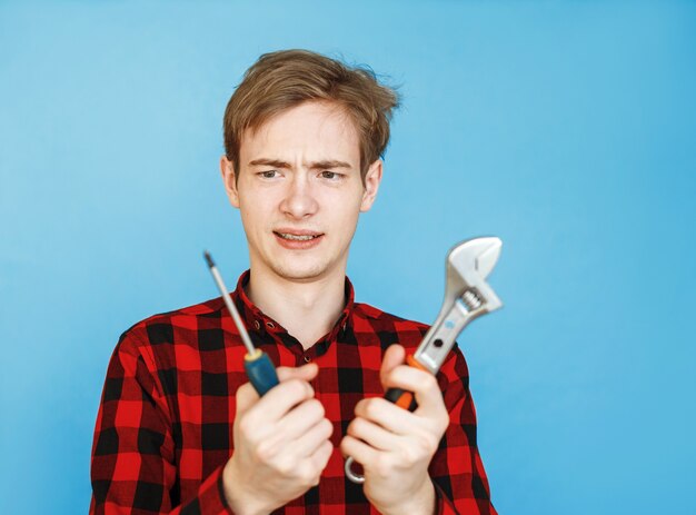 Jeune adolescent de sexe masculin en chemise rouge sur bleu avec des outils tournevis et clé dans la confusion