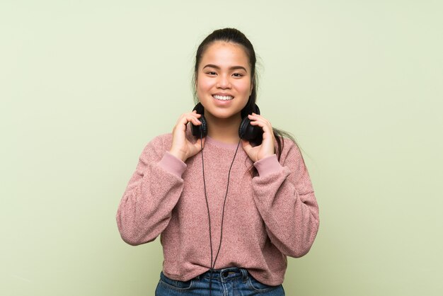 Jeune Adolescente Asiatique Sur Mur Vert Isolé, écouter De La Musique Avec Des écouteurs