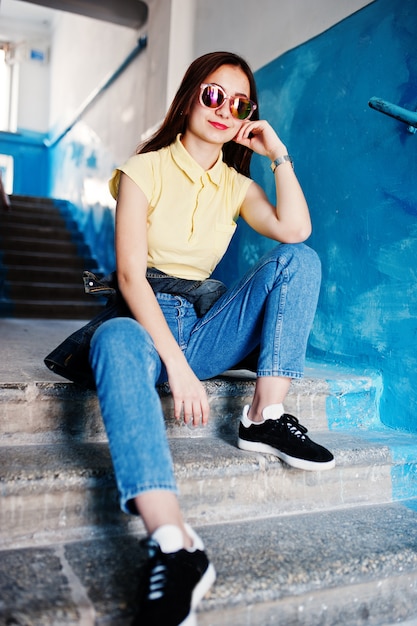 Jeune adolescente assise dans les escaliers de l'entrée de la maison, porter sur un t-shirt jaune, des jeans et des lunettes de soleil.
