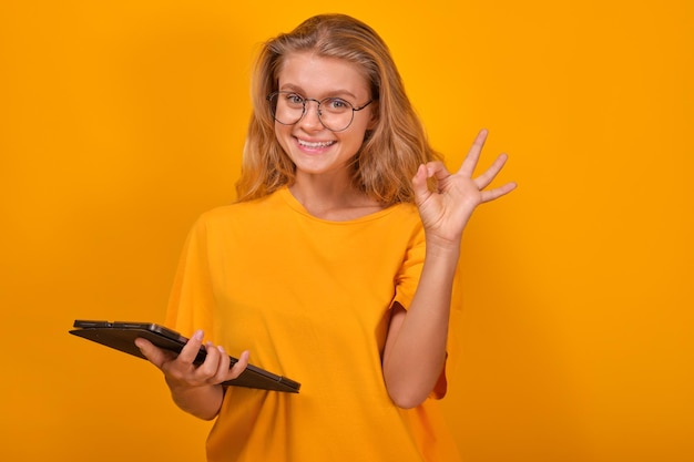 Une jeune adolescente blanche heureuse avec une tablette électronique et fait un geste ok.