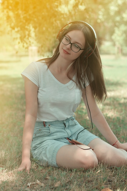 Jeune adolescente écoute de la musique avec des écouteurs et un téléphone intelligent dans le parc, portrait de l'été.