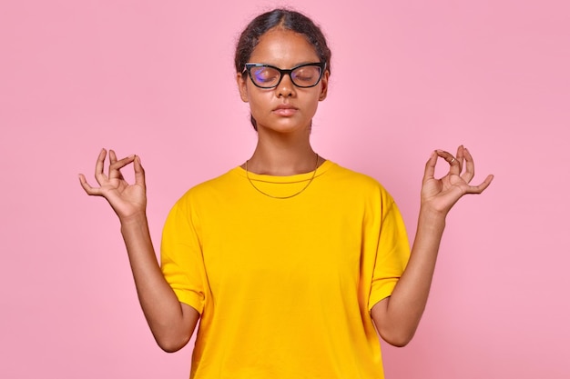 Une jeune adolescente indienne sereine médite avec les mains en l'air et fait un geste mudra