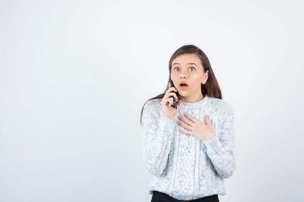 Jeune adolescente parlant sur smartphone sur fond blanc.