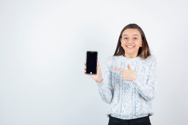 Jeune adolescente pointant sur smartphone sur fond blanc.