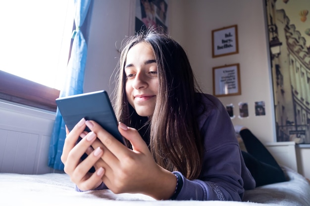 Jeune adolescente se concentre sur la lecture d'un livre électronique avec son lecteur d'ebook sur le lit